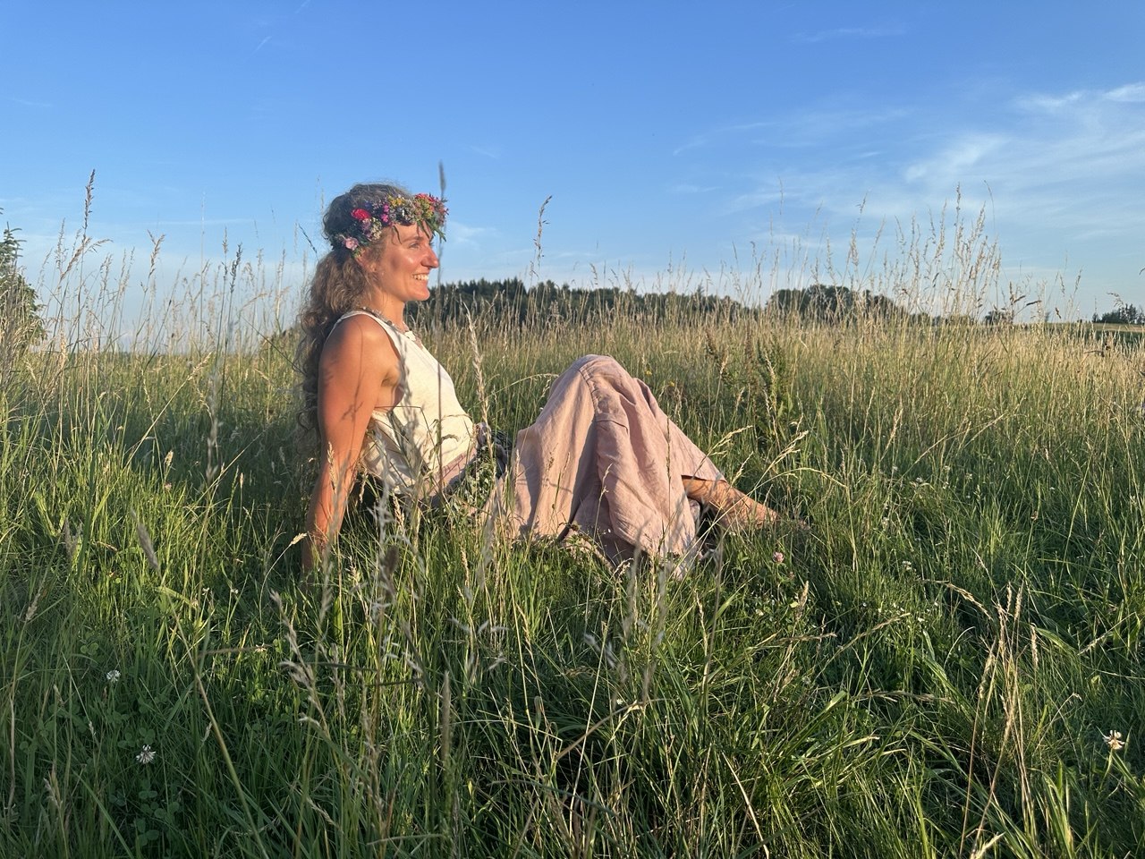 Frau mit Blumenkranz sitzt bei Sonnenuntergang auf einer Sommerwiese in Bad Birnbach.